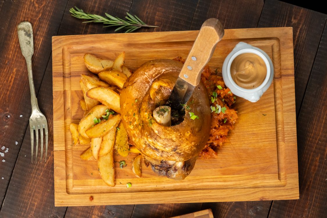 Немецкая рулька с картофельными дольками, тушёной капустой и горчичным соусом на доске